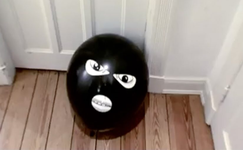 Black balloon with a face placed on the floor in front of a closed door.