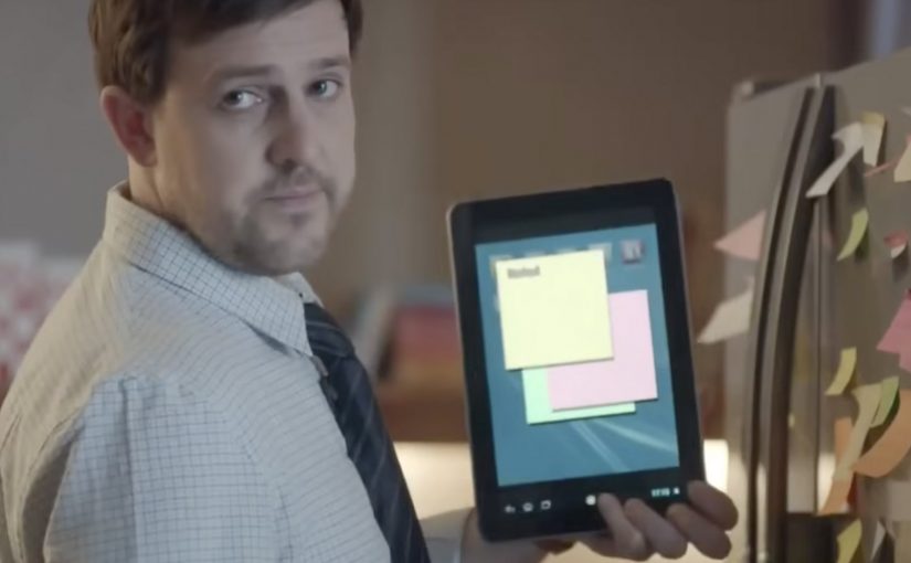 Office worker holds a tablet with digital sticky notes beside a wall covered in paper notes.