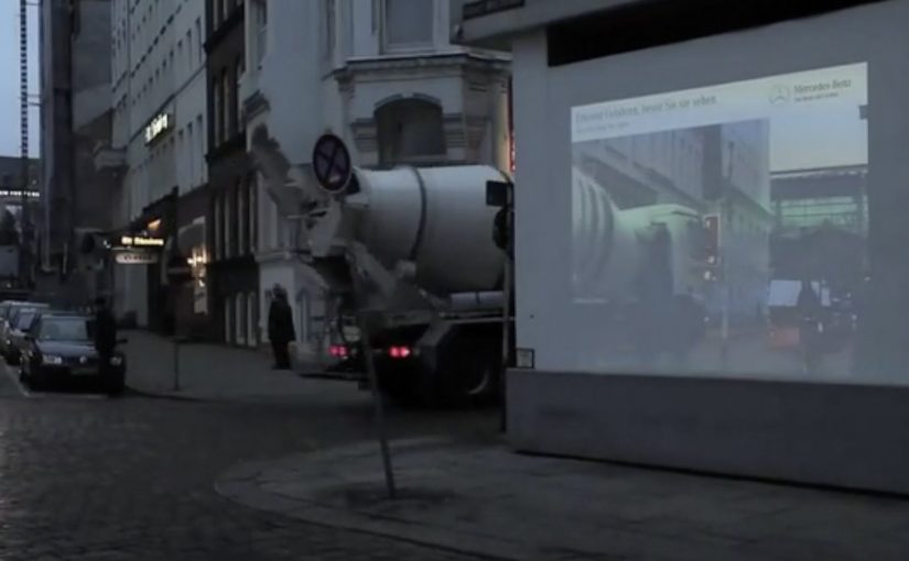 Building-corner billboard projects a live around-the-corner street view for approaching road users.